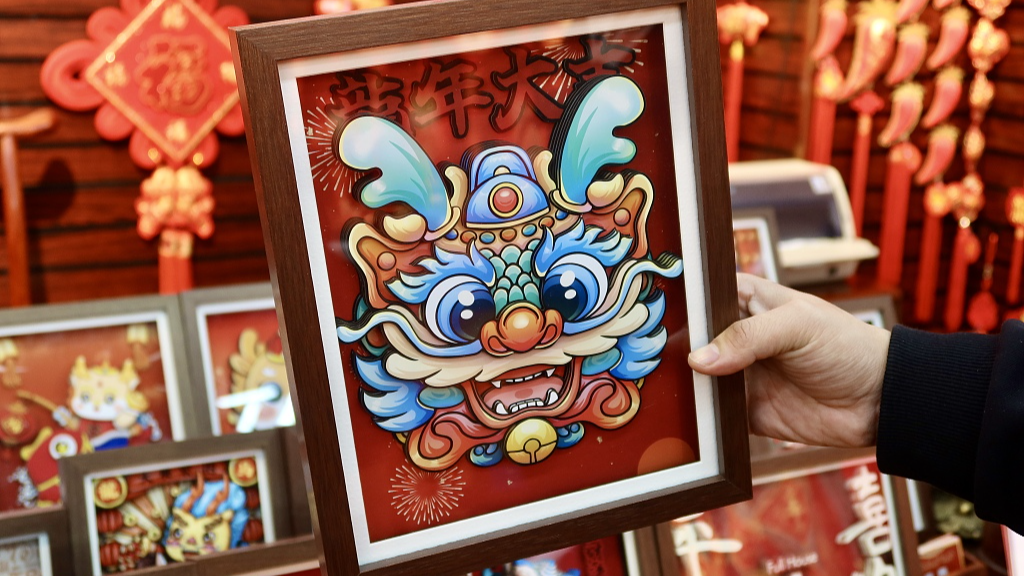 Photo taken on January 3, 2024 shows a stall owner displaying a store's latest loong themed New Year picture ornaments at Yiwu International Trade City in Yiwu, Zhejiang Province. /CFP