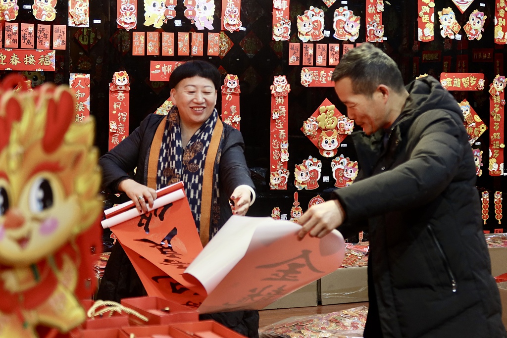 Photo taken on January 3, 2024 shows a stall owner displaying a pair of couplets to a customer in Yiwu, Zhejiang Province. /CFP