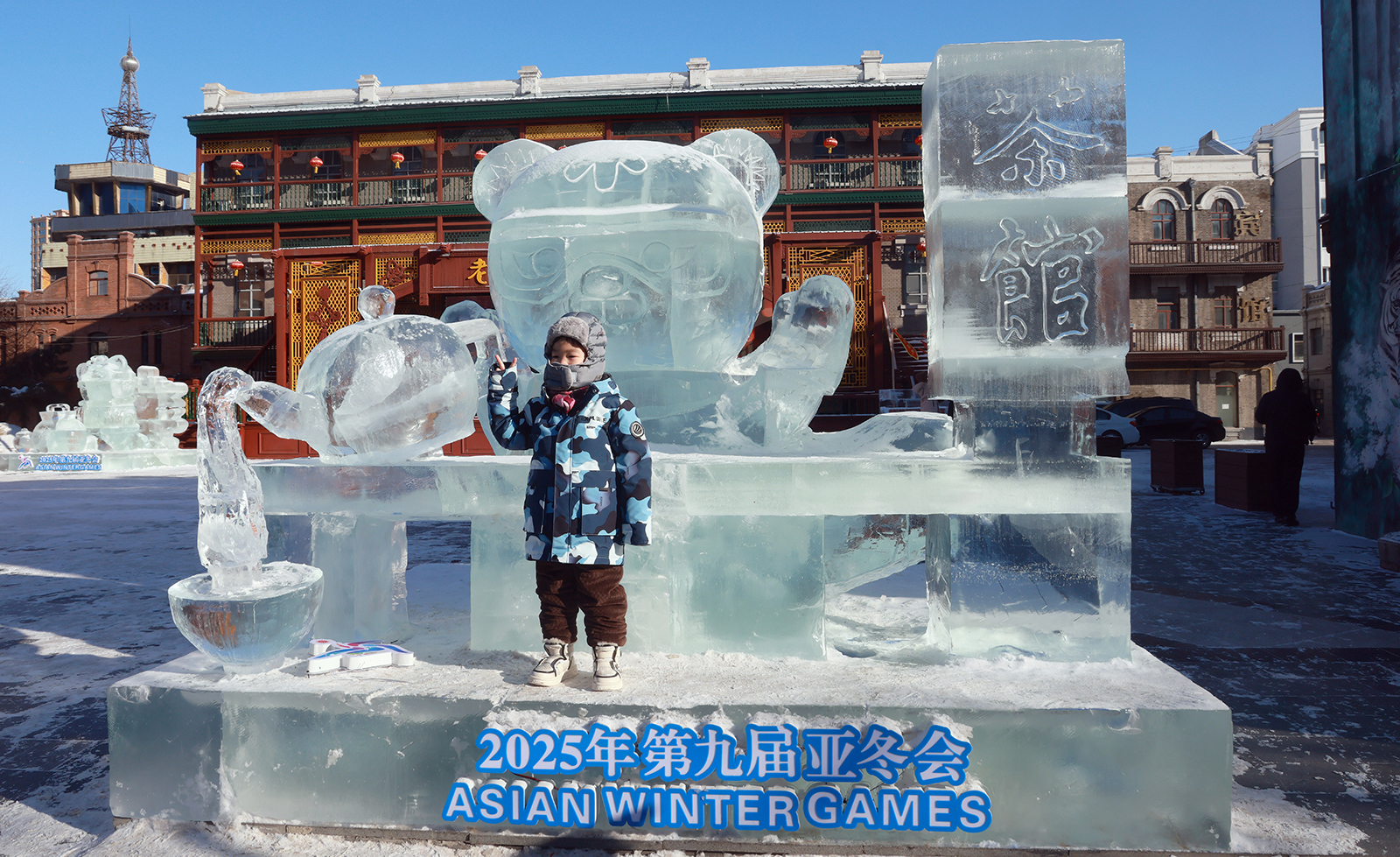 A child poses for photos with an ice sculpture of the Asian Winter Games mascot Binbin holding a teapot at the Laodaowai baroque scenic spot in Harbin, Heilongjiang Province on January 14, 2024. /IC