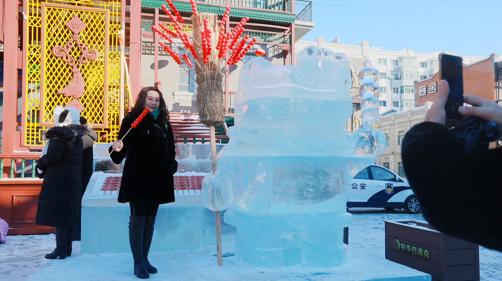 A visitor poses for photos with an ice sculpture of the Asian Winter Games mascot Nini holding tanghulu, or sugar-coated haw sticks, at the Laodaowai baroque scenic spot in Harbin, Heilongjiang Province on January 14, 2024. /IC