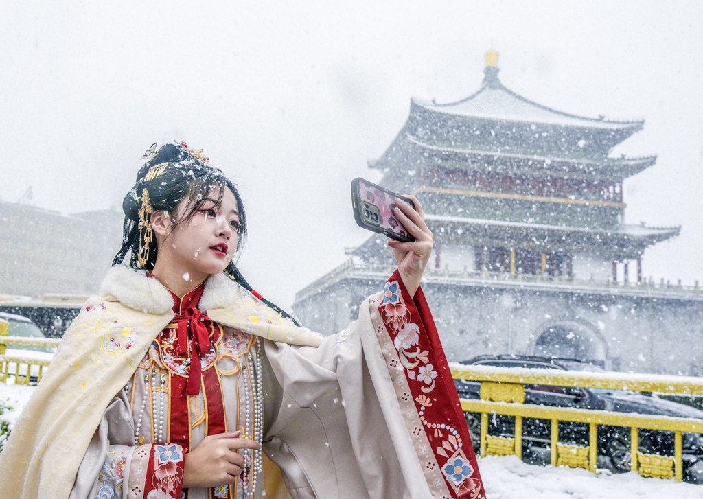 A photo shows a woman taking a selfie at the Xi'an Bell Tower amid snowfall in Xi'an, Shaanxi Province, on January 16, 2024. /IC