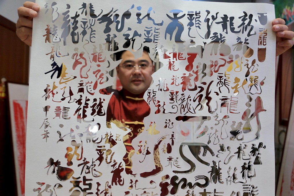 A photo shows paper-cutting practitioner Li Wei holding up a sheet of paper with carved characters and figures at his studio in Lianyungang, Jiangsu Province on January 18, 2024. /CFP