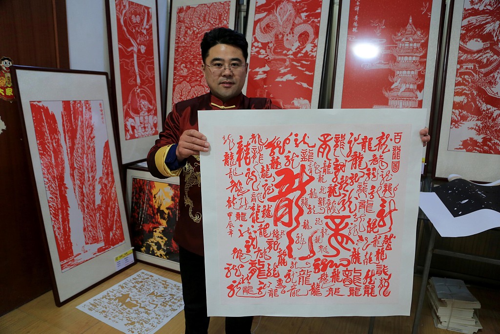 A photo taken January 18, 2024 at a studio in Lianyungang, Jiangsu Province shows paper-cutting practitioner Li Wei holding up a work featuring a number of loong-related characters and symbols. /CFP
