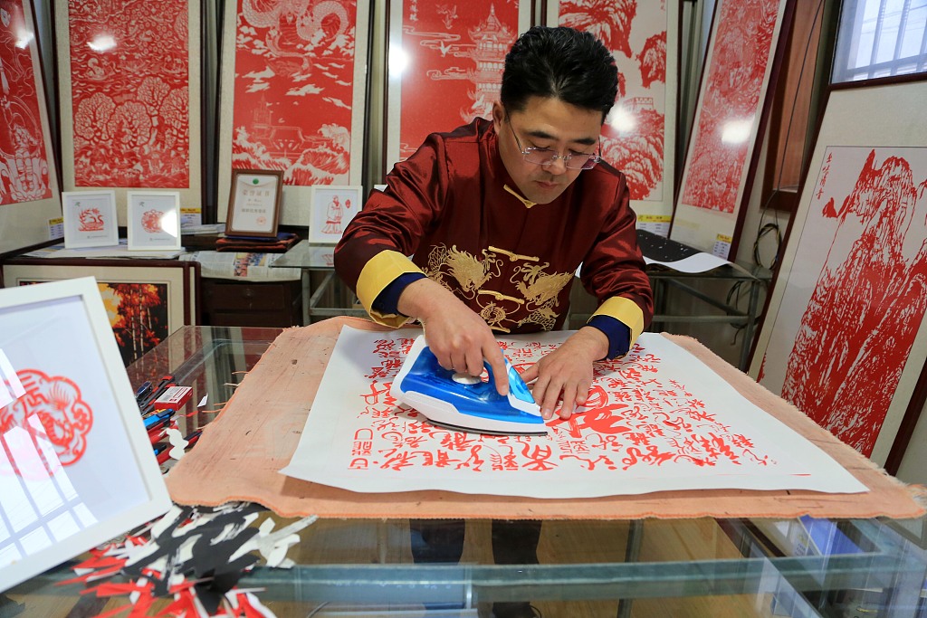 A photo shows paper-cutting practitioner Li Wei using an iron to press his loong-themed work at his studio in Lianyungang, Jiangsu Province on January 18, 2024. /CFP