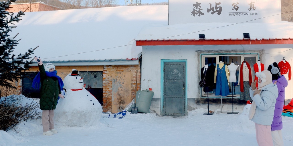 A photo shows a visitor posing for a picture with a snowman in Hengdaohezizhen in Mudanjiang, Heilongjiang Province on January 13, 2024. /IC