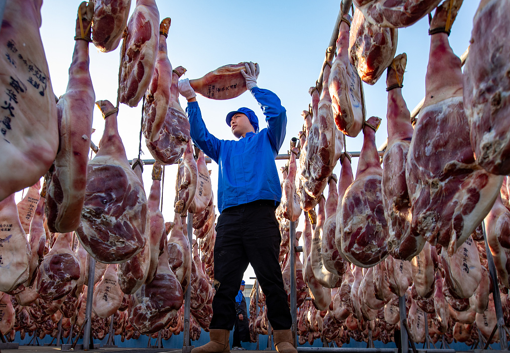 A worker at a factory in Jinhua, Zhejiang Province, hangs dry-cured ham on December 7, 2023. /CFP