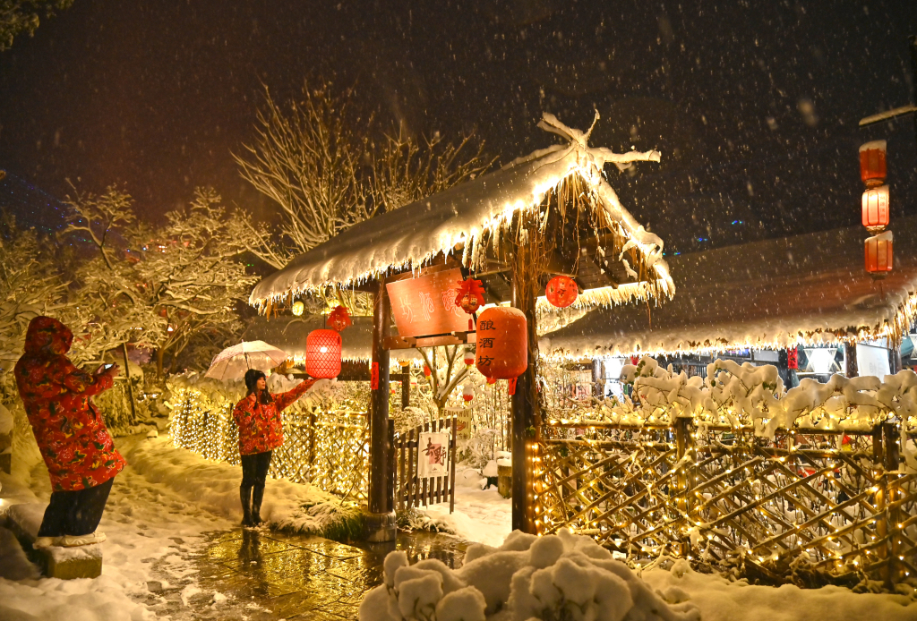 Tourists pose for pictures during nighttime snowfall in Gexian Village in Shangrao, Jiangxi Province on January 22, 2024. /CFP