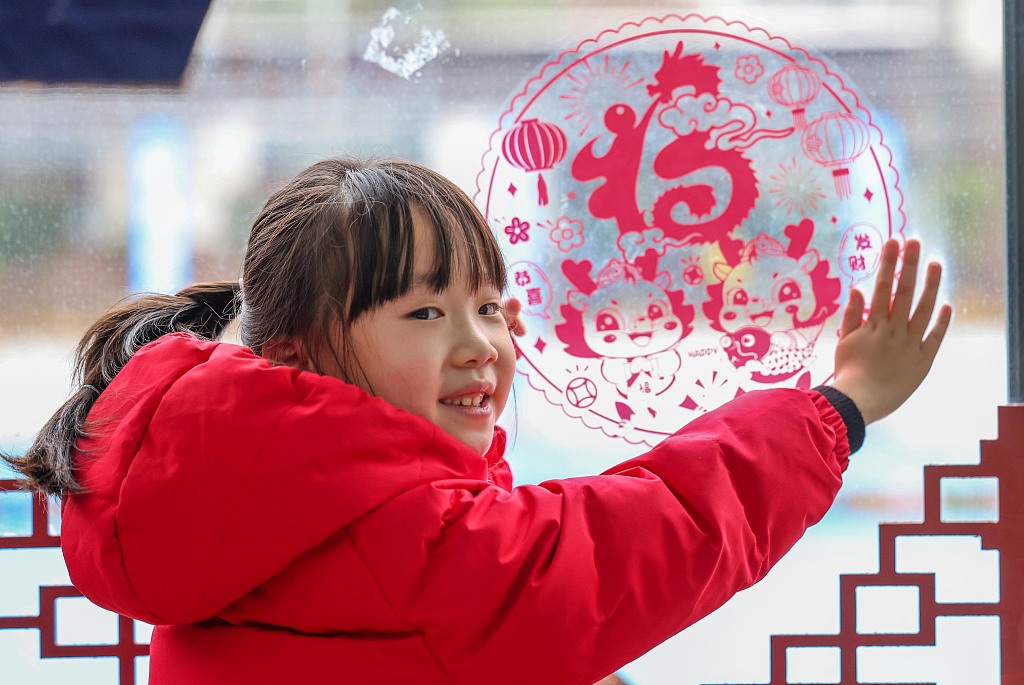 A girl wearing red clothes puts up a piece of window decoration at a kindergarten in Tongren, Guizhou Province to welcome the Spring Festival, January 18, 2024. /CFP