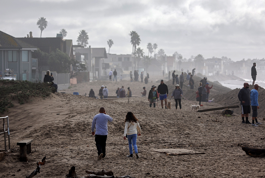 People gather to watch incoming surf behind a newly constructed sand berm to protect against damaging waves, two days after a rogue wave inundated the area and injured eight people in Ventura, California, the U.S., December 30, 2023. /CFP