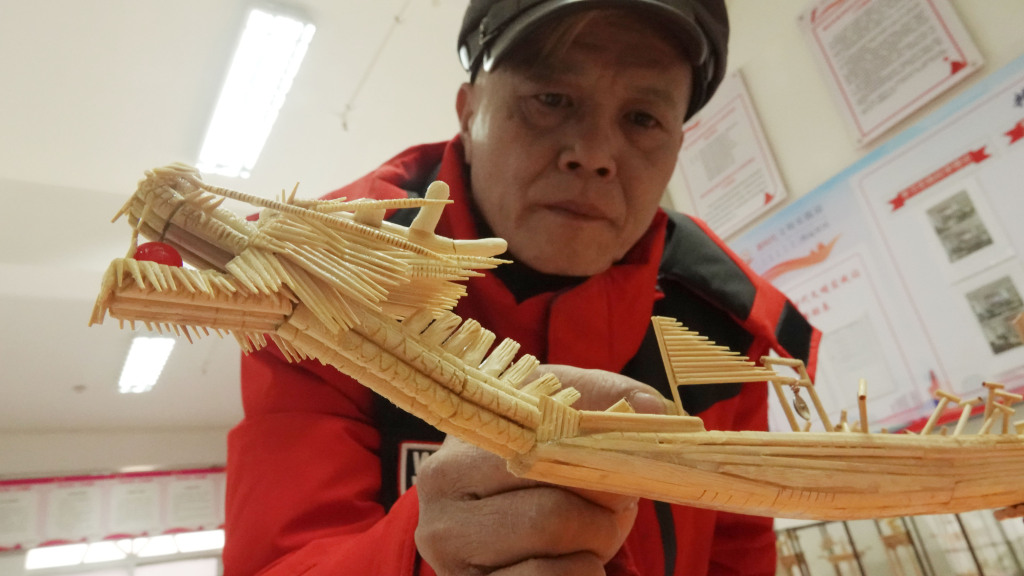 Photo taken on January 24, 2024 in Zhuhai, Guangdong, shows a craftsman examining the bow of a dragon boat model made from upcycled disposable tableware. /CFP