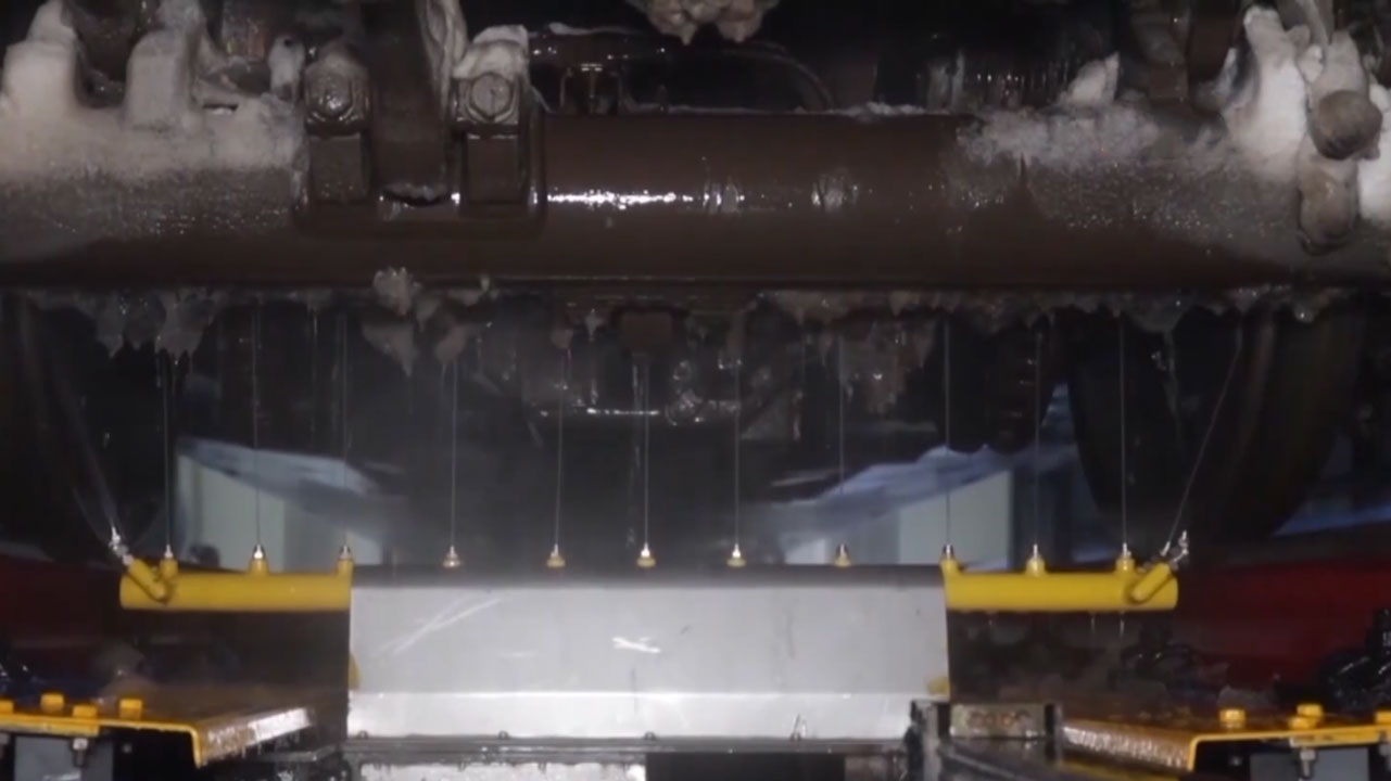 An automated machine cleans the ice under a train car. /CMG