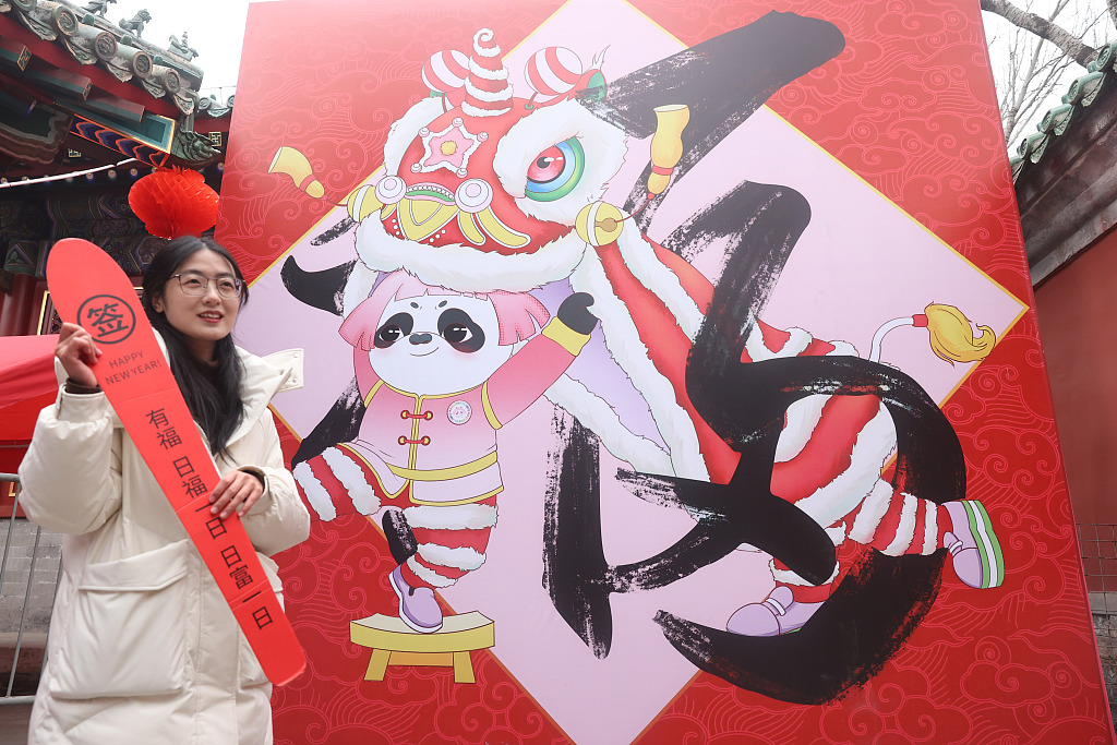 A visitor poses for photos with a Spring Festival-themed backdrop set up for the upcoming traditional temple fair at Ditan Park in Beijing on January 30, 2024. /CFP