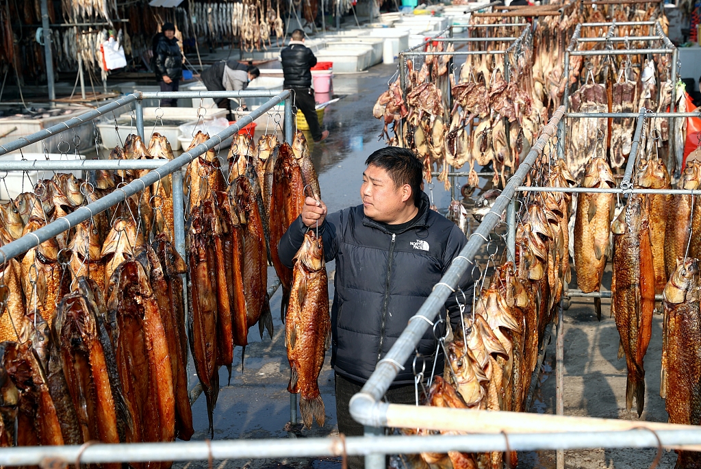 A man checks on fish being sun-dried on racks after seasoning in Suqian, east China’s Jiangsu Province, on January 29, 2024. /CFP