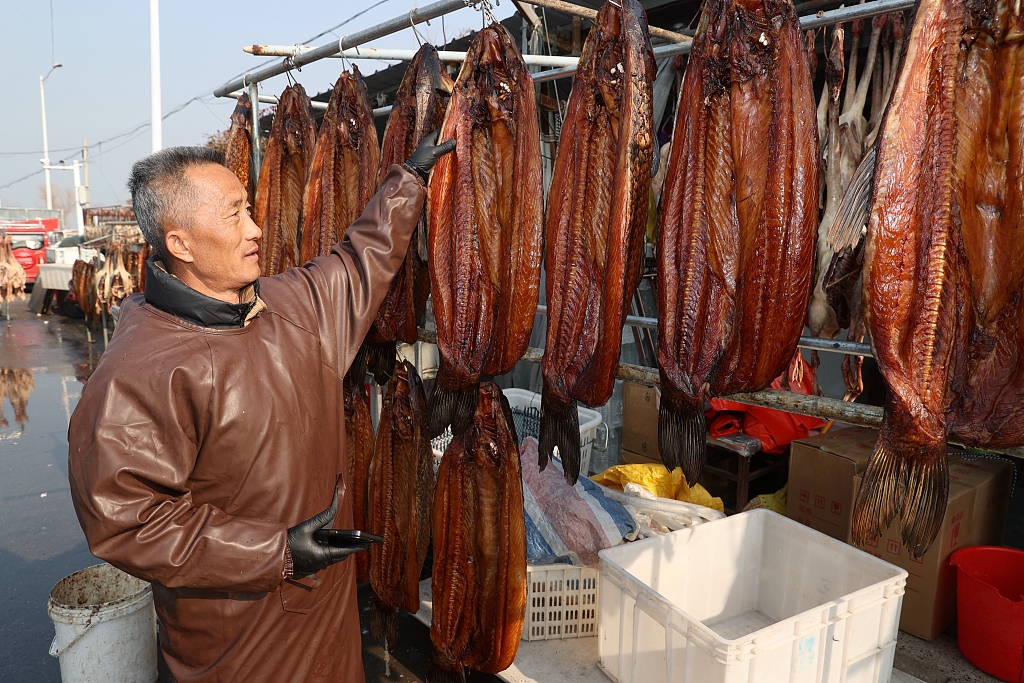 A man checks on fish being sun-dried on racks in Suqian, east China’s Jiangsu Province, January 29, 2024. /CFP