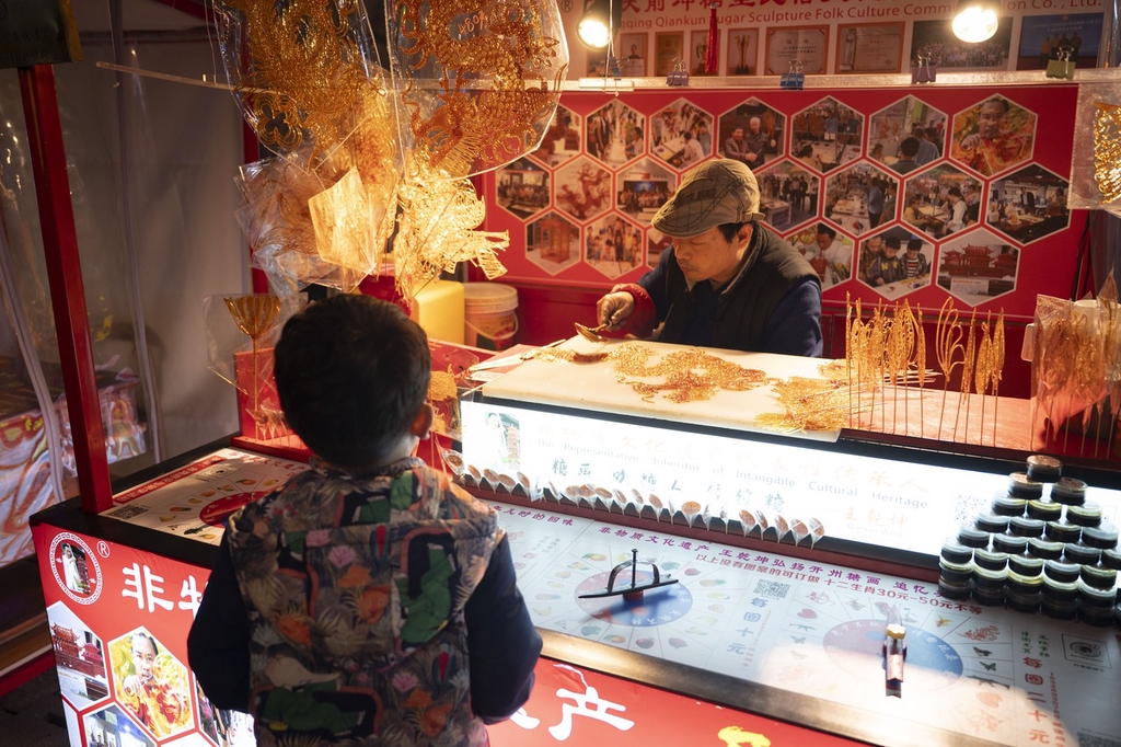 A photo shows a boy watching an artisan making a dragon sugar painting at the Shibati traditional-style scenic area in Chongqing, southwest China, February 5, 2024. /IC