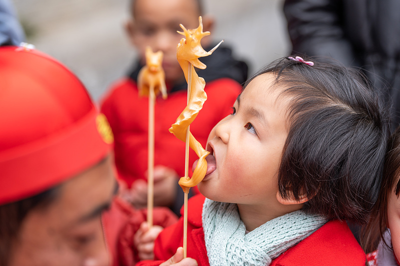 A girl tastes a blown-sugar figurine on a street in Bijie City, Guizhou Province, February 3, 2024. /CFP