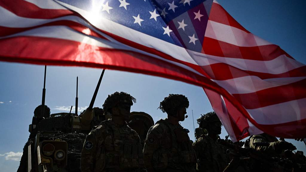 U.S. soldiers stand in formation next to a U.S. flag and a U.S. army armored vehicle as they take part in the NATO 