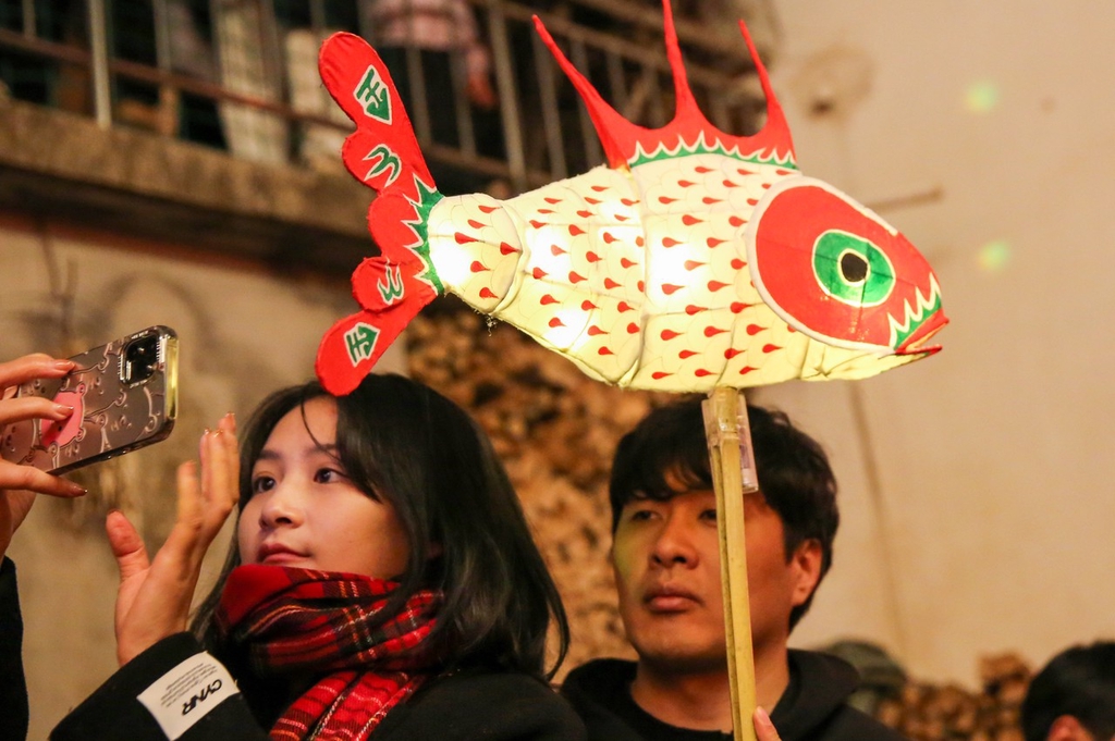 A photo shows a woman taking a selfie near a fish-shaped lantern in the streets of Zhanqi Village in east China's Anhui Province, February 13, 2024. /IC