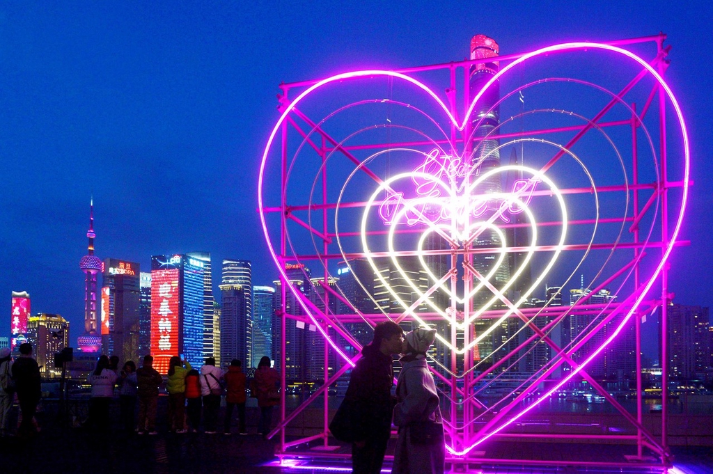 A photo shows a couple kissing in front of a new heart-shaped light installation at the Bund Finance Center in Shanghai, February 13, 2024. /IC