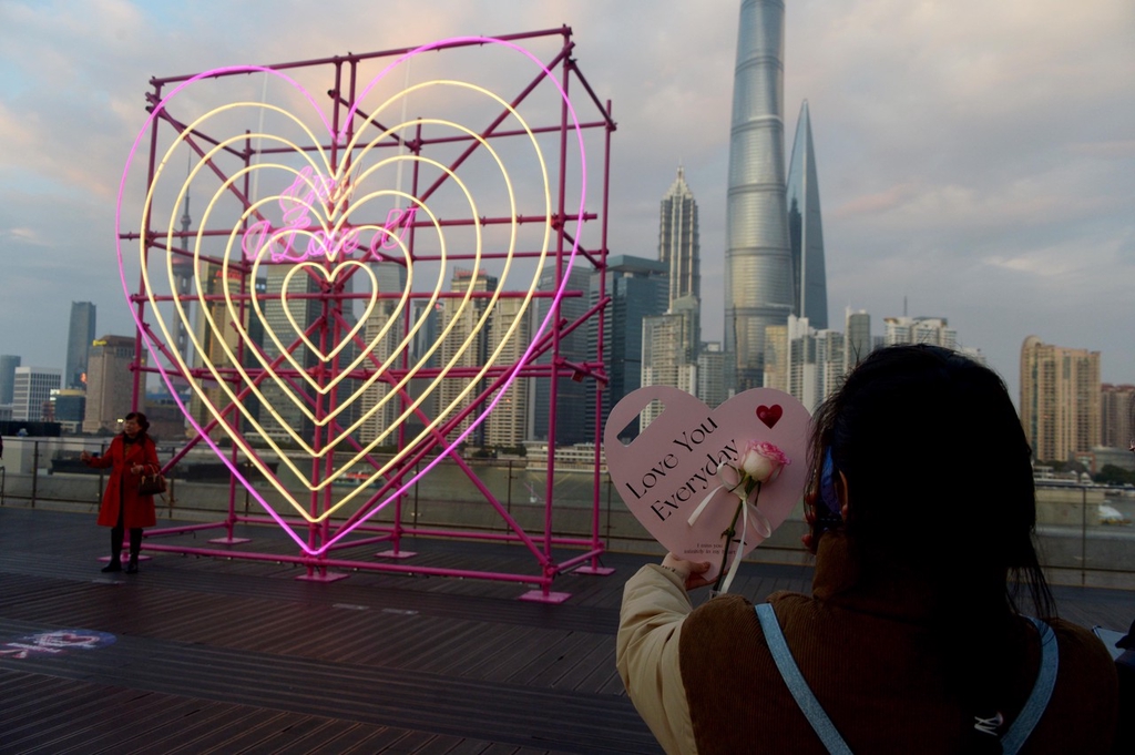 A photo shows a woman holding up a rose and a heart in front of a new heart-shaped light installation at the Bund Finance Center in Shanghai, February 13, 2024. /IC