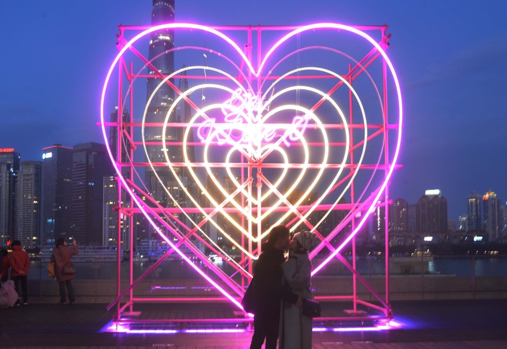 A photo shows a couple stealing a kiss in front of a new heart-shaped light installation at the Bund Finance Center in Shanghai, February 13, 2024. /IC