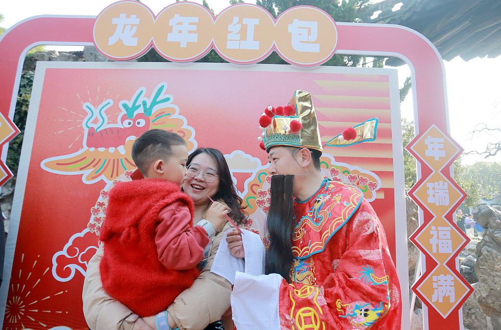 A performer dressed as the God of Wealth (right) sends lucky money to a child in Yangzhou, east China's Jiangsu Province, on February 14, 2024. /CFP