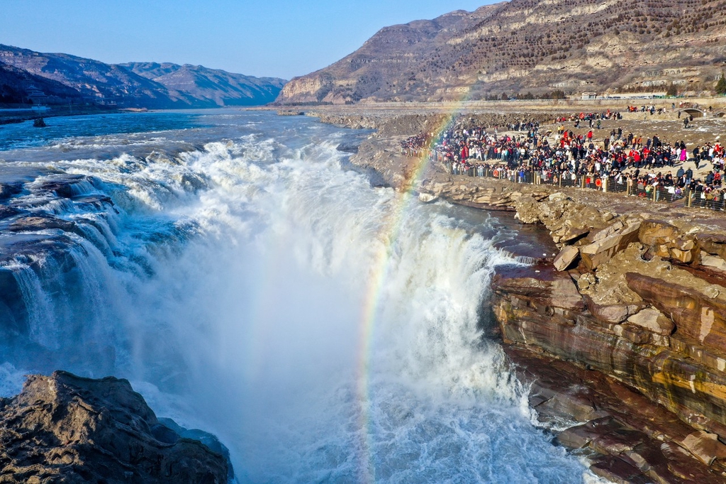 A photo shows visitors admiring a rainbow at the Hukou Waterfall in the intersection of Shanxi and Shaanxi provinces, February 13, 2024. /IC