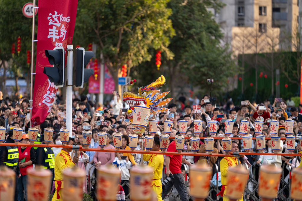 A formation of performers holds a dragon made of wooden benches during the festive parade 