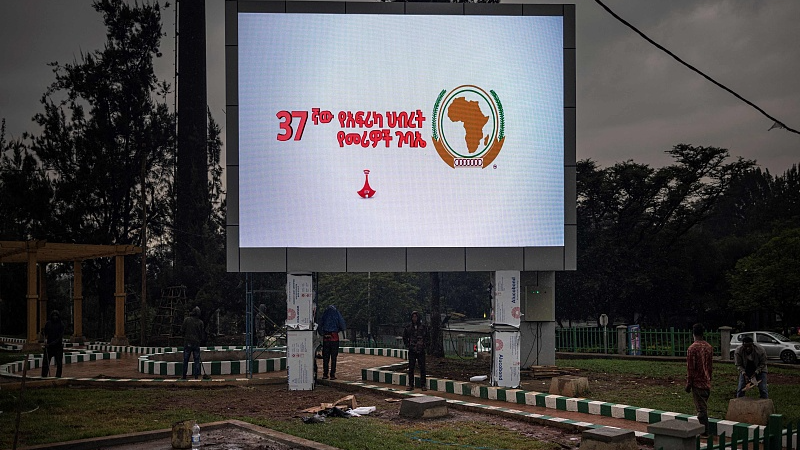 Construction workers shelter from the rain as they finish setting up an electronic sign dedicated to the African Union (AU) in Addis Ababa, February 15, 2024. /CFP