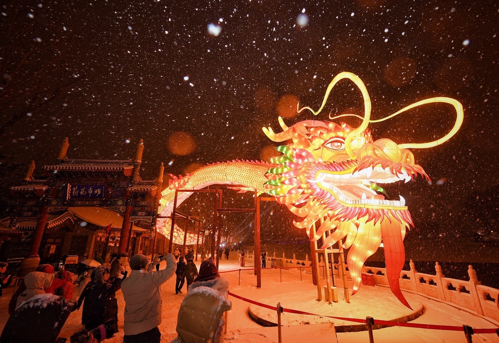 A photo shows people taking pictures of a 200-meter-long dragon lantern during snowfall in the Shichahai shopping area in Beijing, February 20, 2024. /IC