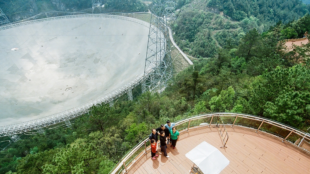 Visitors take pictures with FAST in the background, southwest China's Guizhou Province, April 11, 2023. /CFP