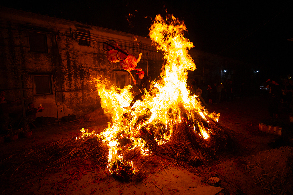 A man holding a lantern leaps through a bonfire as part of a tradition in a village in Meizhou, south China's Guangdong Province, February 21, 2024. /CFP