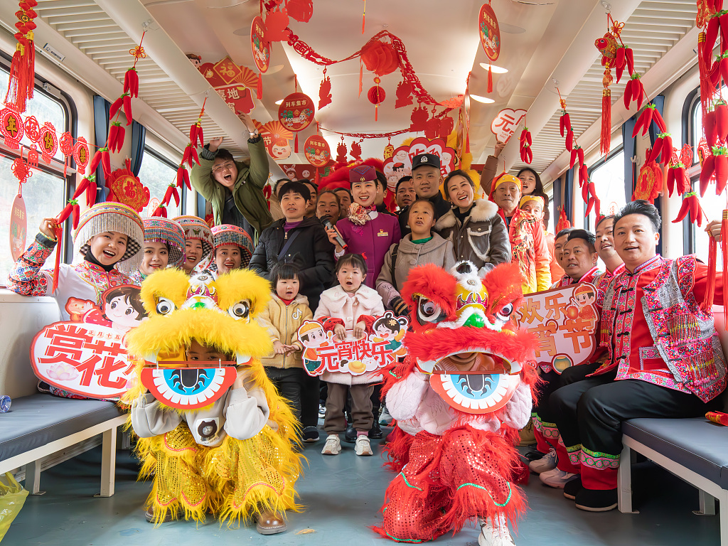 Passengers take photos with performers of a folk culture show onboard a train departing from Zunyi, southwest China's Guizhou Province on February 23, 2024. /CFP