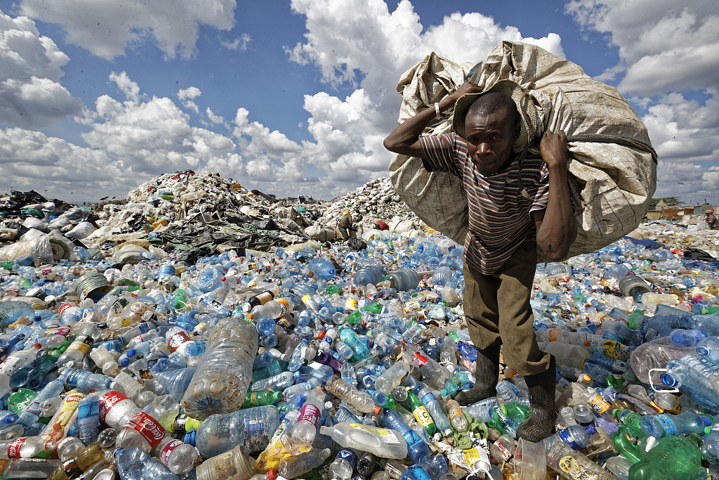 A man walks on a mountain of plastic bottles as he carries a sack of them to be sold for recycling after weighing them at the dump in the Dandora slum of Nairobi, Kenya, December 5, 2018. /CFP