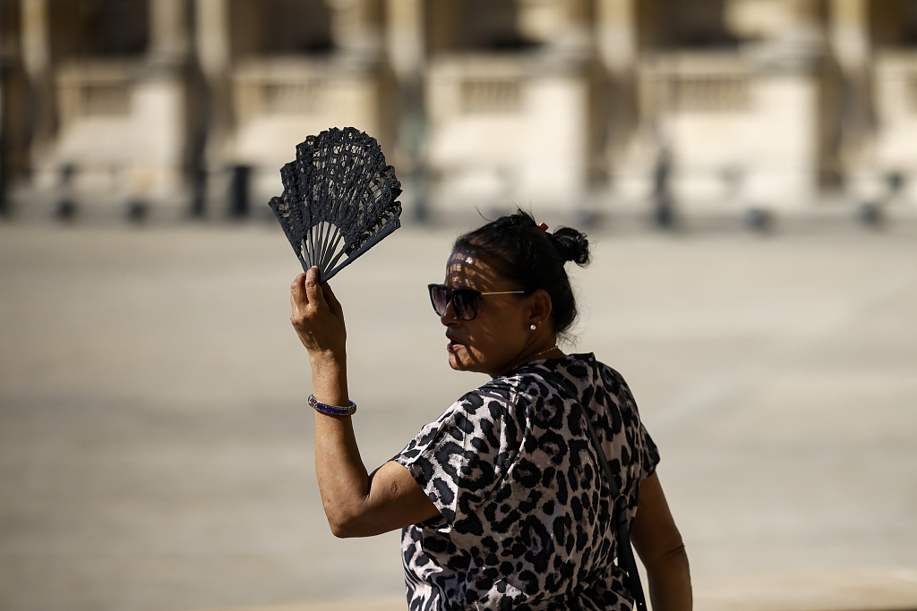 A woman uses a fan in the courtyard of the Louvre Museum in Paris, France, September 7, 2023. /CFP