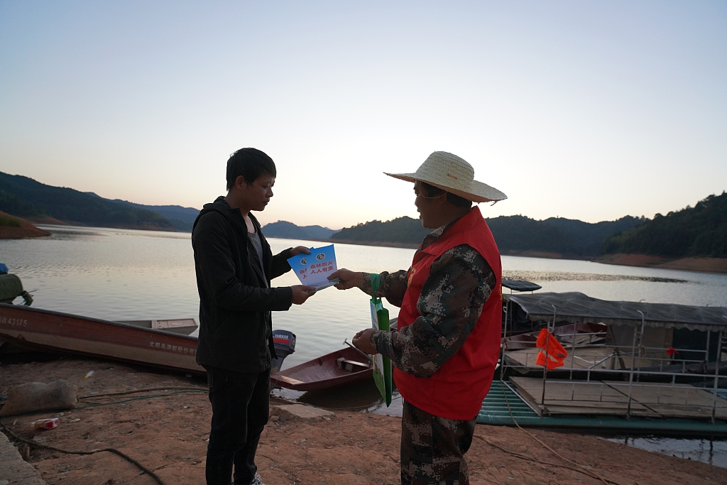 Forest ranger Yang Xingpu gives out a brochure of fire prevention to a tourist at the reservoir area of Shaikou Hydropower Station in the Yudaihe National Wetland Park in Tongdao Dong Autonomous County, central China's Hunan Province, October 15, 2023. /CFP