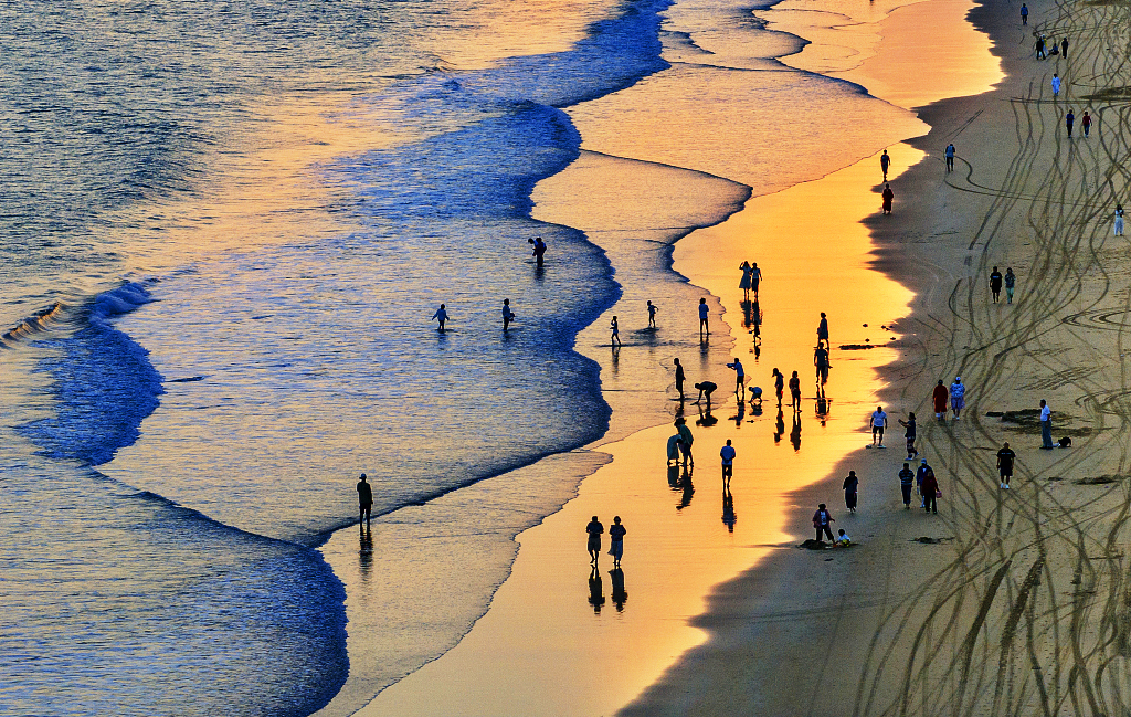 Visitors enjoy the sunrise at Qingshui Bay in Lingshui, Hainan Province, as the morning tide and beach are bathed in golden sunlight on February 28, 2024. /CFP