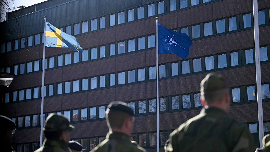 Swedish soldiers look on as the NATO flag (R) is hoisted next to the Swedish flag in front of the headquarters of Sweden's Armed Forces in Stockholm, Sweden, March 11, 2024. /CFP
