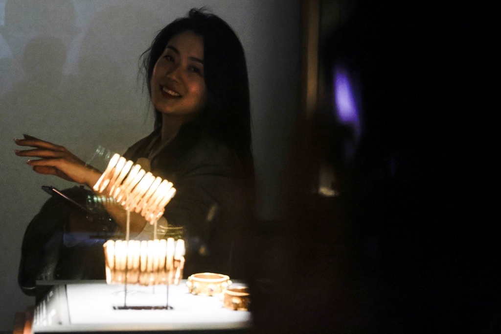 A woman poses for a picture behind sets of gold bangles that form part of an exhibition of relics from the tomb of Ming Dynasty Prince Liangzhuang, on display at Hubei Provincial Museum, Wuhan, Hubei Province, March 12, 2024. /IC