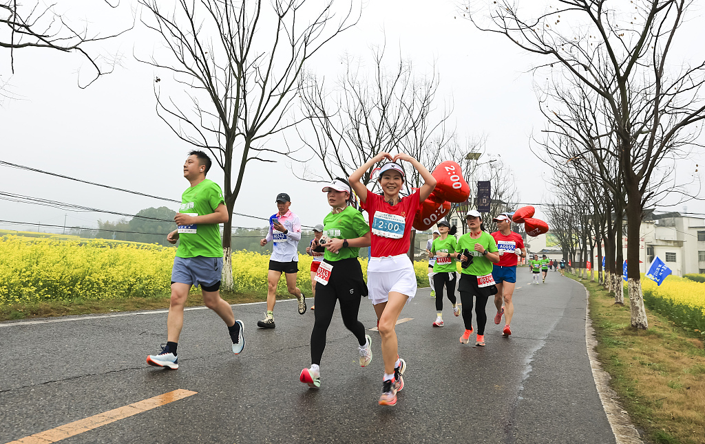 Runners run along a road lined with rape flowers in Ruichang, east China's Jiangxi Province, March 17, 2024. /CFP 