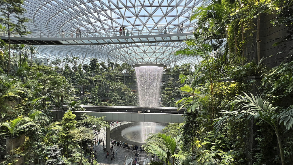 A 40-meter-high circular indoor waterfall pours into the building from the roof as passengers walk and take pictures at Changi Airport, a glass circular building surrounded by hanging terraced gardens, in Singapore, October 4, 2023. /CFP