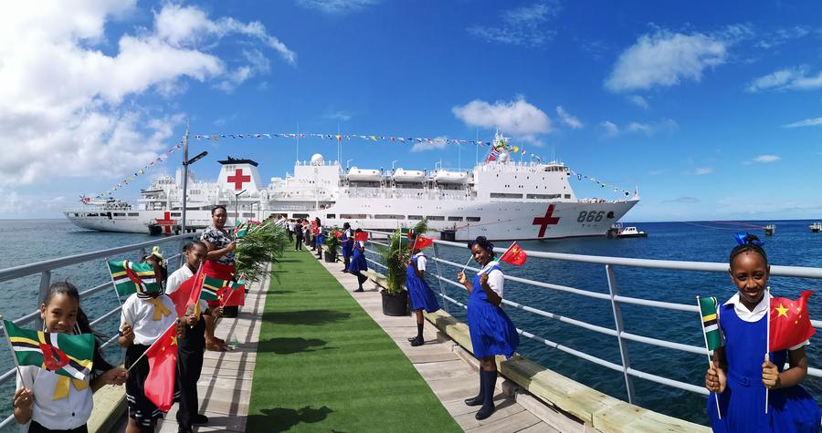 Local students wave national flags of China and the Commonwealth of Dominica to greet the first arrival of the Chinese People's Liberation Army (PLA) Navy hospital ship Peace Ark in Roseau, Commonwealth of Dominica, October 12, 2018. /Xinhua