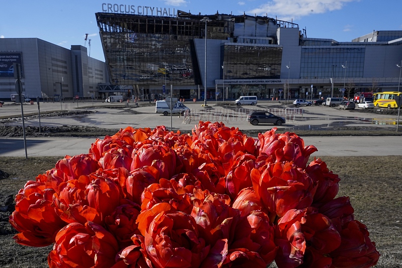 A bouquet of flowers inserted into the road fence in front of the burnt Crocus City Hall, center, on the western outskirts of Moscow, Russia, March 27, 2024. /CFP