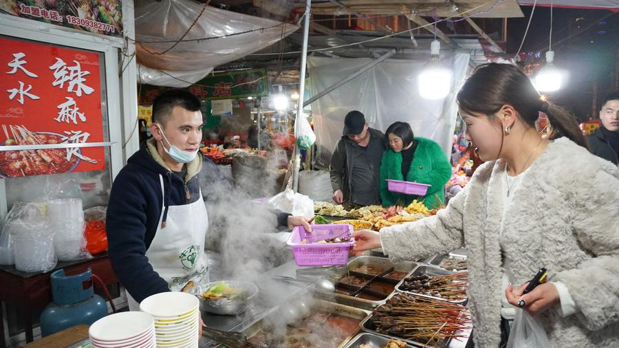 An owner of a malatang stall serves a customer on a snack street in Qinzhou District of Tianshui City, northwest China's Gansu Province, March 19, 2024. /Xinhua