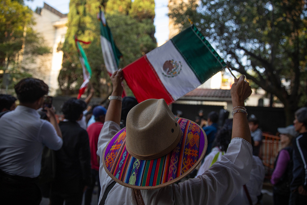 A woman holds a Mexican flag while police officers stand guard outside the embassy of Ecuador in Mexico during a protest following the arrest of former Ecuadorian Vice President Jorge Glas in Mexico City, Mexico, April 6, 2024. /CFP