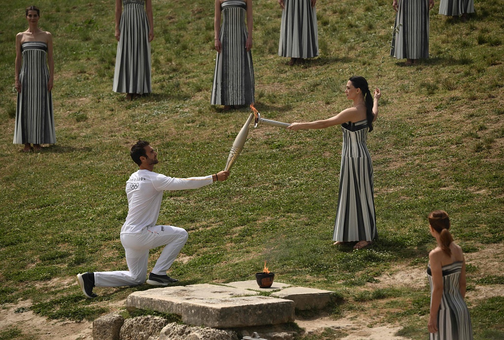 Greek actress Mary Mina (R) lights the Olympic torch in the hands of the country's Olympic gold medalist competitive rower Stefanos Ntouskos in front of the ruins of the Temple of Hera in Olympia, Greece, April 16, 2024. /CFP