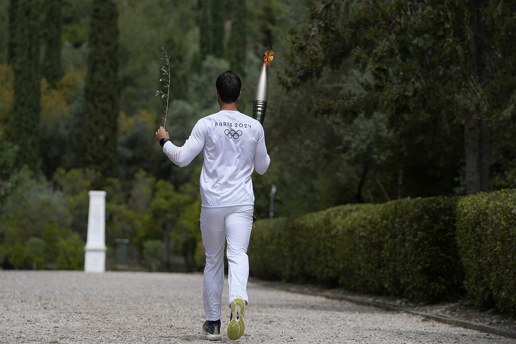 Competitive rower and Greek Olympic gold medalist Stefanos Ntouskos carries the Olympic torch in his right hand and the olive branch, symbolizing peace, in his left at the ruins of the Temple of Hera in Olympia, Greece, April 16, 2024. /CFP