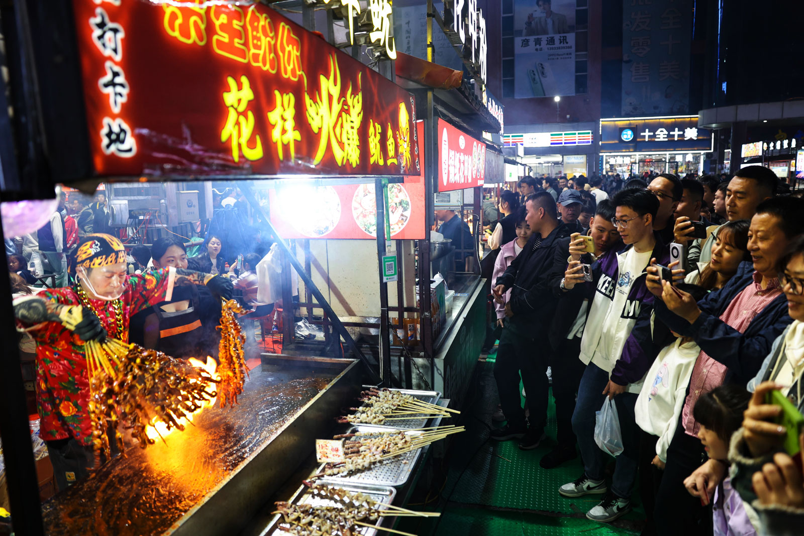Visitors take videos as a stallholder grills kebabs over a strong fire at the night market at the Zhengding International Small Commodities Market in Hebei Province on April 14, 2024. /IC
