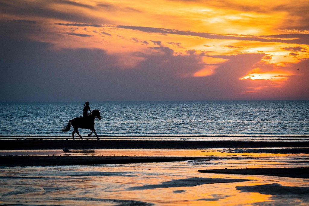 A person rides a horse as the sun sets on the beach of Deauville, France. /CFP