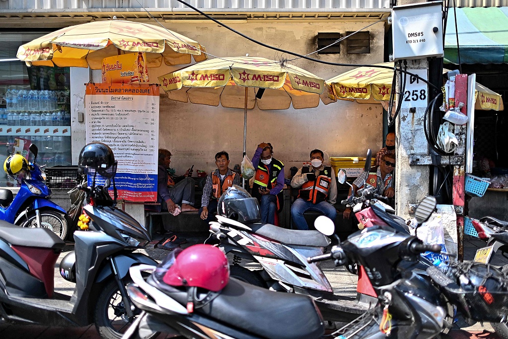 Motorbike taxi drivers take shelter from the sun under big umbrellas as they wait for customers in Bangkok, Thailand, April 25, 2024. /CFP